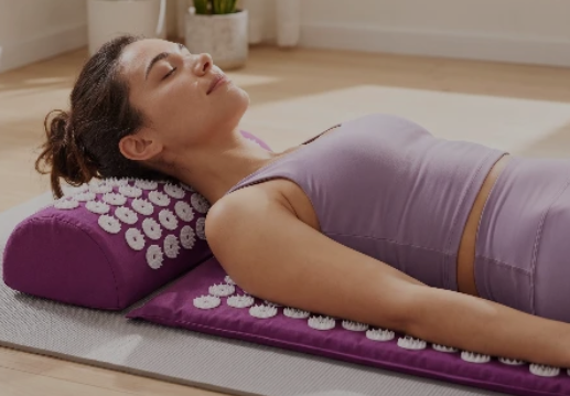 Woman lying on a purple acupressure mat with flower designs on a wooden floor.